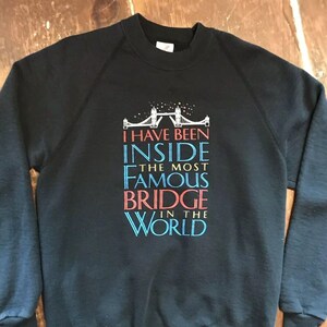 Op de afbeelding: Zwart sweatshirt met een afbeelding van de Tower Bridge in Londen en de tekst "Ik ben in de beroemdste brug ter wereld geweest".