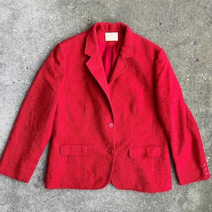 Op de afbeelding: Een rode blazer met een enkele knoopsluiting en twee zakken. De blazer is gemaakt van een getextureerde stof.