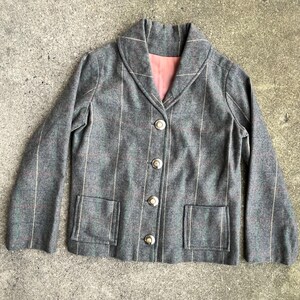 May include: A gray plaid blazer with a wide collar and button closure. The blazer has two pockets on the front and a pink lining.