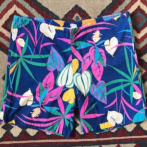 May include: Blue shorts with a vibrant tropical leaf pattern in pink, green, yellow, and white. The shorts have a classic cut and a comfortable fit, perfect for warm weather. The fabric appears to be a lightweight cotton or blend.