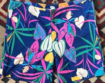 May include: Blue shorts with a vibrant tropical leaf pattern in pink, green, yellow, and white. The shorts have a classic cut and a comfortable fit, perfect for warm weather. The fabric appears to be a lightweight cotton or blend.