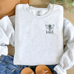 May include: A gray sweatshirt with a black bee and the word "kind." embroidered on the front.