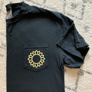 May include: Black t-shirt with a yellow embroidered sunflower on a pocket.