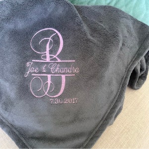 May include: A gray fleece blanket with a pink embroidered monogram of the letters "B" and "J" with the text "Joe & Chandra" and the date "7.30.2017" underneath.