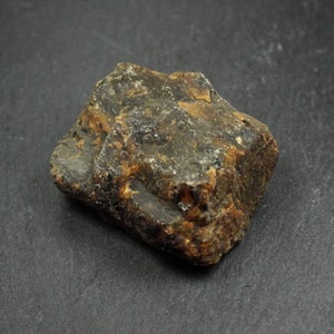May include: A rough, irregularly shaped stone with a mix of dark brown, black, and amber hues. The surface has a textured appearance, with visible ridges and variations in color. The stone is likely a natural mineral or gemstone.