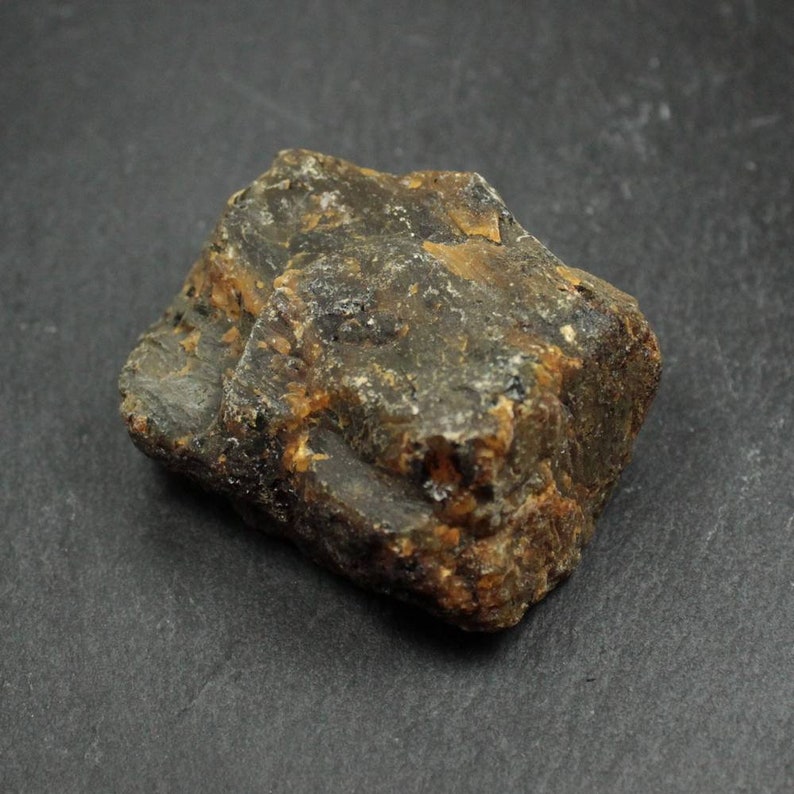 May include: A rough, irregularly shaped stone with a mix of dark brown, black, and amber hues. The surface has a textured appearance, with visible ridges and variations in color. The stone is likely a natural mineral or gemstone.