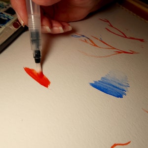 Puede incluir: Una mano sosteniendo un pincel con pintura roja, pintando un trazo rojo en un papel blanco. Hay una acuarela azul en el fondo.