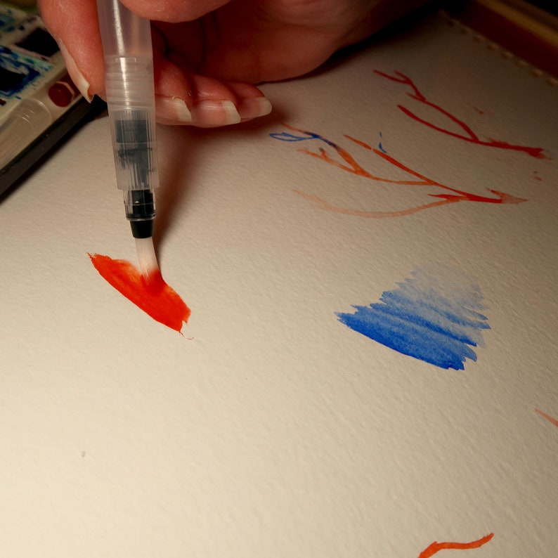 Puede incluir: Una mano sosteniendo un pincel con pintura roja, pintando un trazo rojo en un papel blanco. Hay una acuarela azul en el fondo.