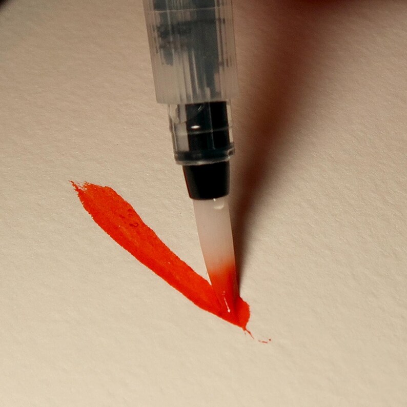 Puede incluir: Primer plano de una pincelada roja de acuarela hecha con un bol&iacute;grafo pincel. El bol&iacute;grafo pincel es transparente con una punta negra y un pincel blanco.