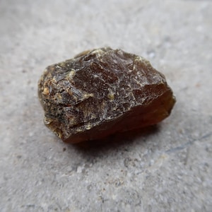 May include: A rough, amber-colored stone with a textured surface. The stone has a natural, irregular shape and varying shades of brown and yellow. The image is a close-up, highlighting the details of the mineral.