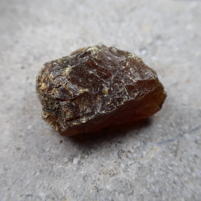 May include: A rough, amber-colored stone with a textured surface. The stone has a natural, irregular shape and varying shades of brown and yellow. The image is a close-up, highlighting the details of the mineral.
