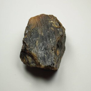 May include: A rough, irregularly shaped amber-colored stone with dark brown and black streaks. The surface has a textured, layered appearance, with variations in color and opacity. The stone is likely a natural mineral specimen.