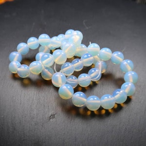 May include: Several strands of light blue opalite gemstone beads. The beads are round and have a milky, translucent appearance. The beads are strung together, forming bracelets. The opalite beads are a soft, pastel blue colour.
