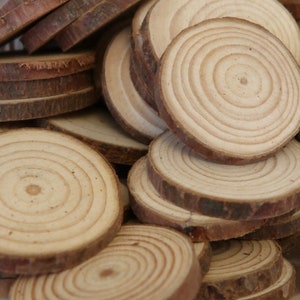 May include: A pile of natural wood slices, each with a circular shape and concentric rings. The wood is a light brown colour and has a smooth, polished finish.