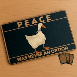 Pode incluir: Uma placa de metal retangular com acabamento envelhecido. Apresenta um ganso branco com uma faca no bico, sobre um fundo azul escuro. O texto "PEACE WAS NEVER AN OPTION" é exibido em negrito. Três cartas colecionáveis são visíveis.