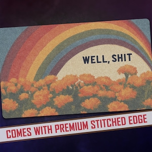 May include: Rectangular doormat featuring a rainbow arching over a field of orange flowers. The words "WELL, SHIT" are printed in black. The bottom of the mat has the text "COMES WITH PREMIUM STITCHED EDGE".