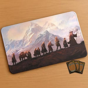 Puede incluir: Alfombrilla de ratón rectangular con un paisaje de fantasía. La ilustración muestra figuras ascendiendo una montaña. Se ve un grupo de personajes, incluido un mago, subiendo una colina. El fondo muestra montañas nevadas y una puesta de sol. Se ven tres cartas coleccionables.