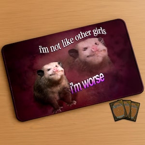 Op de afbeelding: Een rechthoekige, donkerrode muismat met twee opossum-afbeeldingen en de tekst "I'm not like other girls, I'm worse" in wit en roze. Drie ruilkaarten zijn zichtbaar in de rechter benedenhoek.
