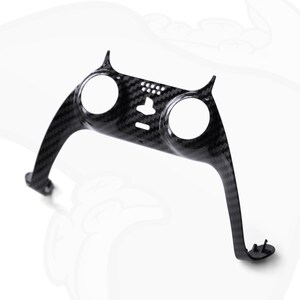 Op de afbeelding: Een zwart carbonfiber interieurbekledingstuk voor auto's met twee ronde uitsparingen. Het bekledingstuk is ontworpen om rond de dashboardbedieningselementen te passen.