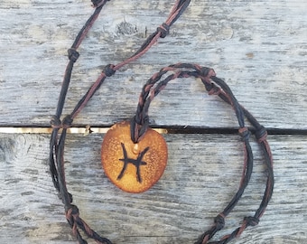 May include: A brown leather cord necklace with a wooden pendant featuring the Pisces zodiac symbol.