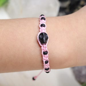 May include: Pink braided bracelet with black skull beads.