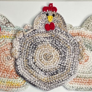 May include: Three crocheted chicken pot holders in different color combinations. The pot holders are round with a scalloped edge and feature a red crocheted beak and wattle.