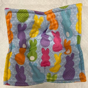 Könnte beinhalten: Ein blauer, gesteppter Topflappen mit einem Muster aus bunten Osterhasenformen. Die Hasen sind in verschiedenen Farben, darunter rosa, lila, grün, orange und gelb.