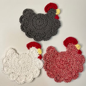 May include: Three crocheted chicken coasters. One is grey, one is white, and one is red and white.