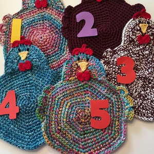 Könnte beinhalten: Fünf gehäkelte Hühner-Topflappen in verschiedenen Farben. Die Topflappen sind von 1 bis 5 nummeriert.