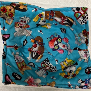May include: A blue fabric pot holder with a quilted design featuring various dogs wearing glasses. The dogs are in different poses and have different coloured glasses. The fabric has a white background with black bones and the words "Bow Wow Mom" and "I Love Dogs" printed on it.