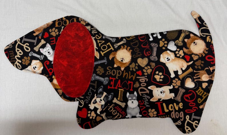May include: A dog-shaped fabric item with a black background, featuring various dog illustrations, paw prints, hearts, and the words "I Love Dog" and "Love My Dog." It has a large red ear.