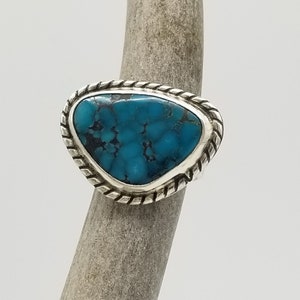 May include: A sterling silver ring featuring a vibrant turquoise stone. The stone is a striking shade of blue with dark matrix patterns. The ring has a twisted rope design around the bezel, adding a classic touch to the jewelry.