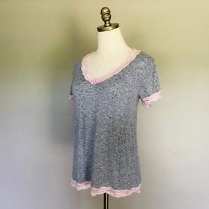 May include: A gray and white polka dot shirt with a pink lace trim around the neckline and sleeves. The shirt has a V-neck and short sleeves.