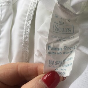 May include: White cotton blend fabric with a white lace trim. The fabric has a label that reads "Sears Perma-Prest Needs No Ironing 65% Kodel Polyester 35% Cotton Exclusive of Decoration RN 14676 505".