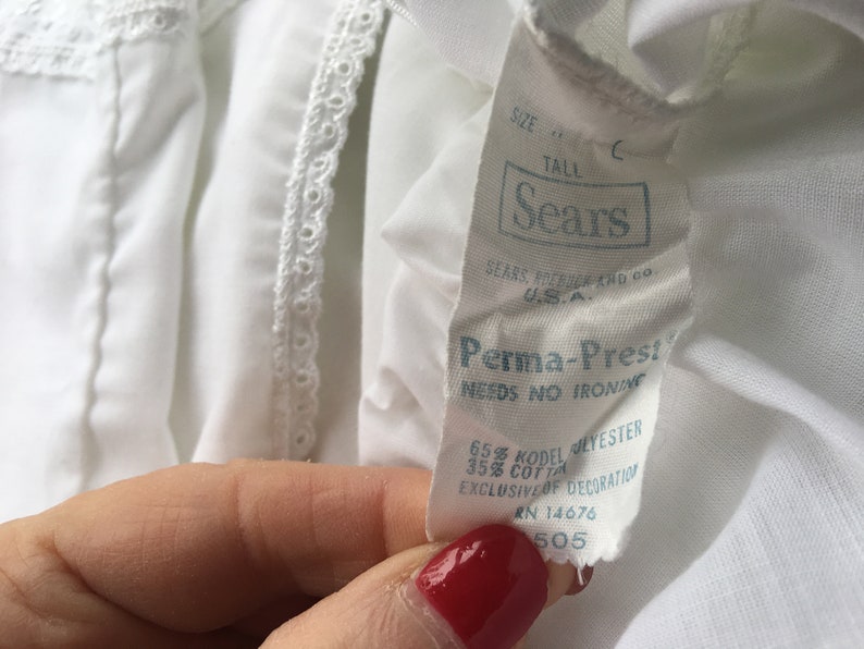 May include: White cotton blend fabric with a white lace trim. The fabric has a label that reads "Sears Perma-Prest Needs No Ironing 65% Kodel Polyester 35% Cotton Exclusive of Decoration RN 14676 505".