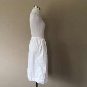 May include: A white slip skirt with a lace trim. The skirt is on a white mannequin.