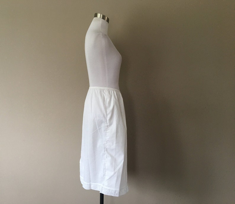 May include: A white slip skirt with a lace trim. The skirt is on a white mannequin.