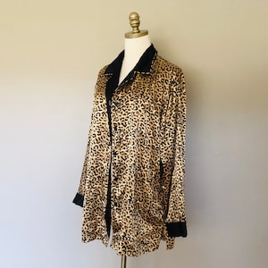 May include: A long-sleeved robe with a leopard print pattern and black trim. The robe has a button closure and a collar.