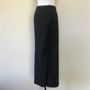 Op de afbeelding: Zwarte broek met wijde pijpen en een omgeslagen zoom. De broek is gemaakt van een effen, donkere stof en heeft een klassiek, getailleerd ontwerp. De broek wordt op een mannequin gepresenteerd.