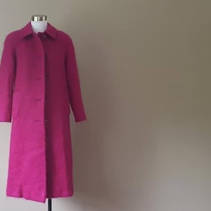 May include: A long, fuchsia-colored coat with a button closure. The coat is made of a fuzzy, textured fabric.