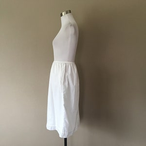 May include: A white cotton slip skirt with a gathered waistband. The skirt is knee-length and has a simple, classic design.