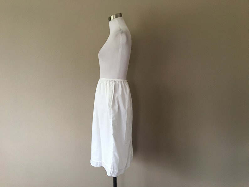 May include: A white cotton slip skirt with a gathered waistband. The skirt is knee-length and has a simple, classic design.