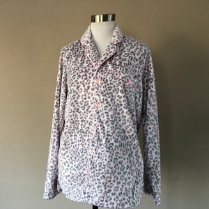 Puede incluir: Una camisa de manga larga con botones y estampado de leopardo rosa y gris. La camisa tiene cuello y un bolsillo en el lado izquierdo.