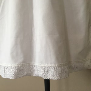 May include: White cotton slip with a delicate lace trim. The lace is a white floral pattern.