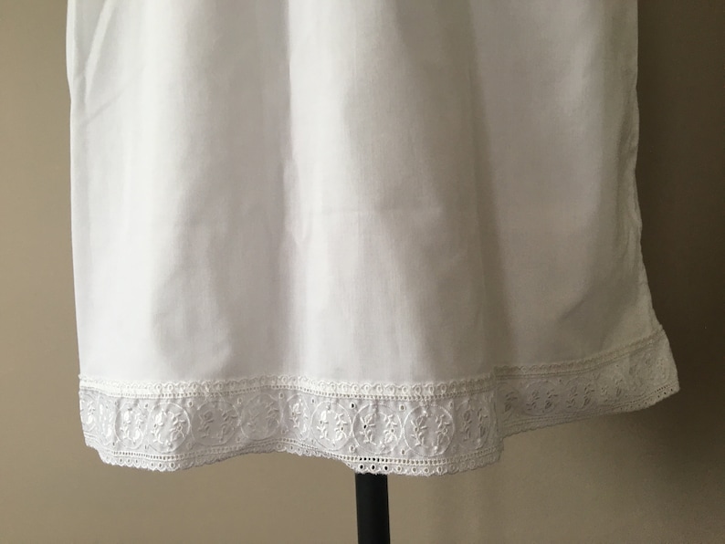 May include: White cotton slip with a delicate lace trim. The lace is a white floral pattern.