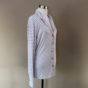 May include: A long-sleeved, striped button-down shirt in a light blue and white color scheme. The shirt has a relaxed fit and a collar.