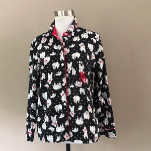 May include: Black pajama top with a white polar bear pattern and red trim. The long-sleeved shirt has a button-down front, a breast pocket with a red embroidered design, and a red-lined collar.