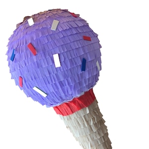 May include: A purple ice cream cone pi&ntilde;ata with red, white, and blue confetti. The cone is made of beige paper fringe, and the top is a sphere of purple paper fringe. A fun party decoration.