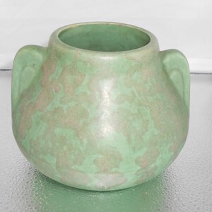 May include: A green ceramic vase with two handles. The vase has a mottled glaze with a light green and white pattern.