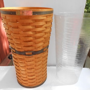 May include: A tall, woven basket with a dark brown band and a clear plastic container. The basket is made of light brown wicker and has a small rectangular tag. The container has measurement markings.
